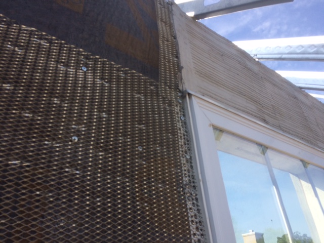 Se muestra un acercamiento del sistema de control de lluvia Driwall Rainscreen, un perfil metálico galvanizado a lo largo de la ventana y un listón de metal instalado con parte de la capa de adherencia encima de la ventana.